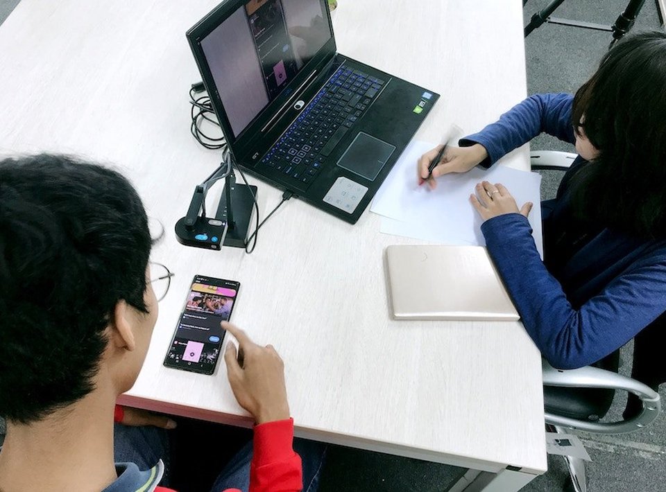 A person looking at a mobile device while another person observes and takes notes